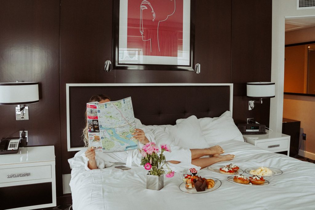 Lady lying down on a hotel bad with a big map and breakfast platters on the bed