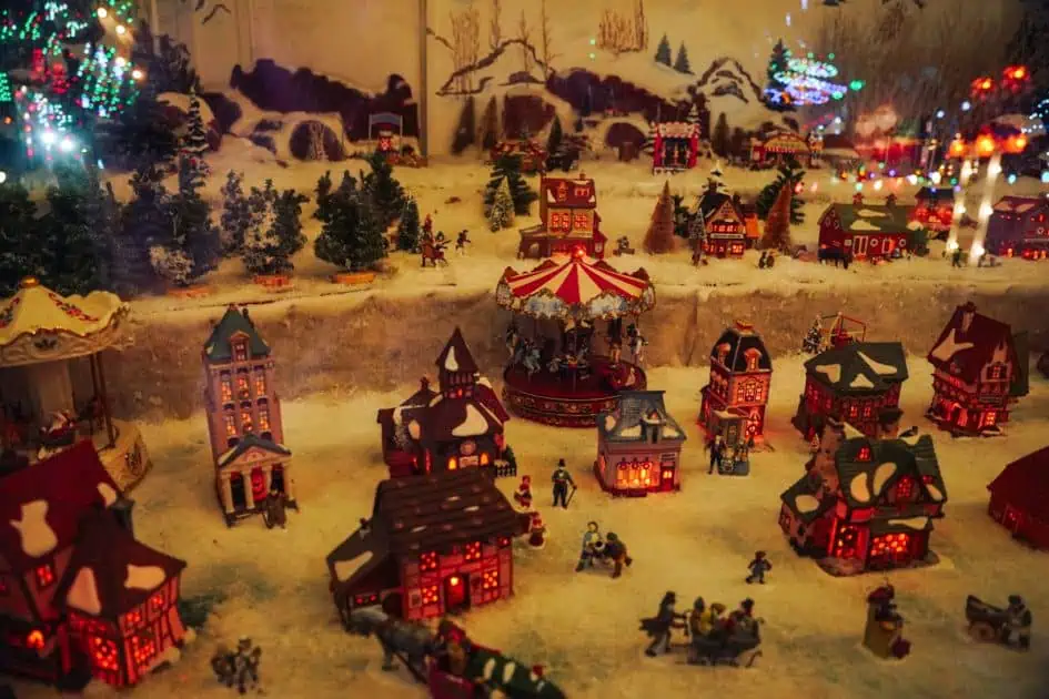 Window display at Koziars Christmas Village featuring a cozy village with houses, carousel, trees and people 